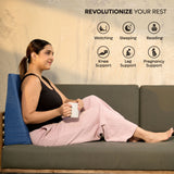 Woman sitting on couch using ADMIRAE memory foam wedge pillow for back support while holding a mug