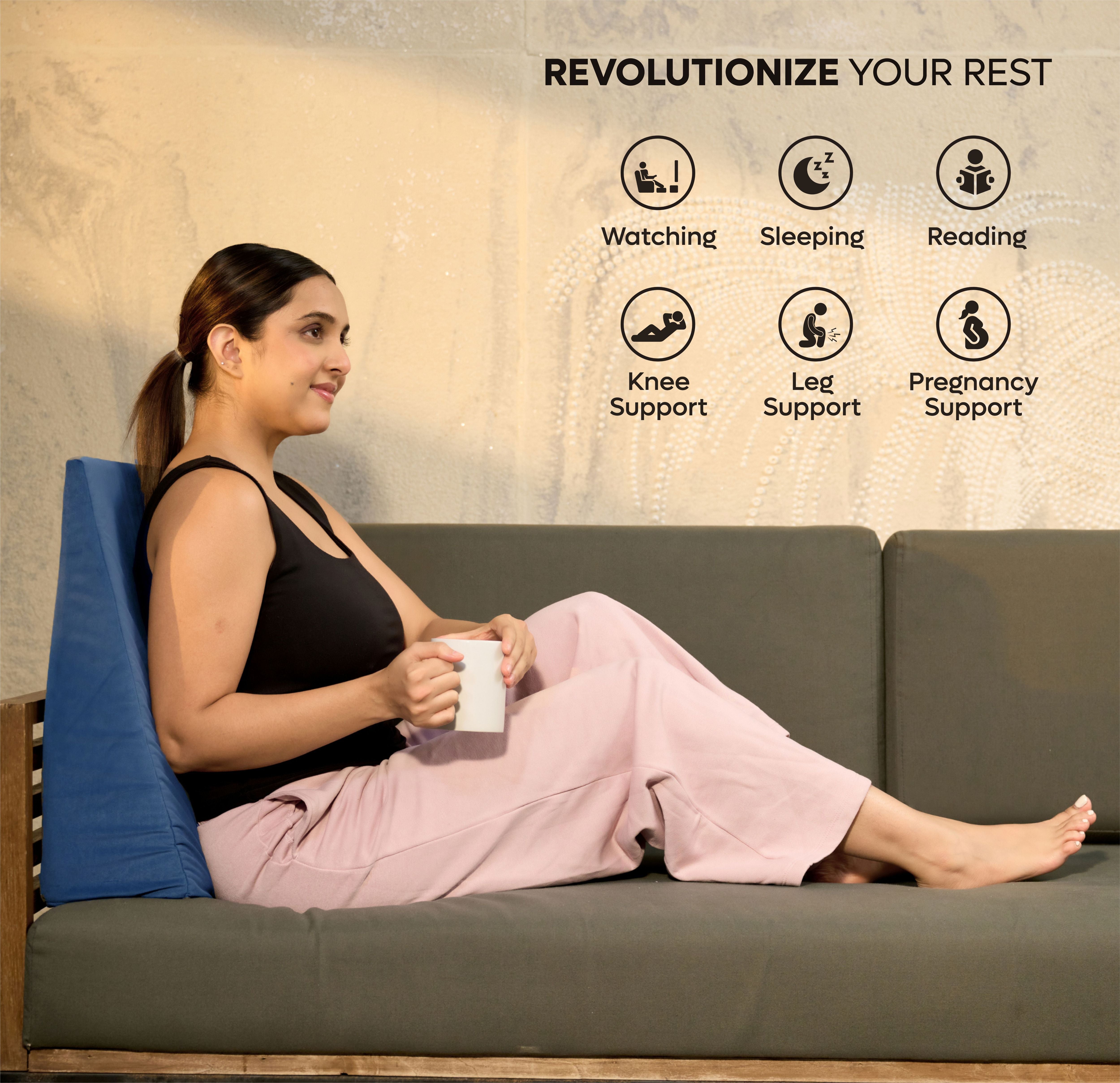 Woman sitting on couch using ADMIRAE memory foam wedge pillow for back support while holding a mug